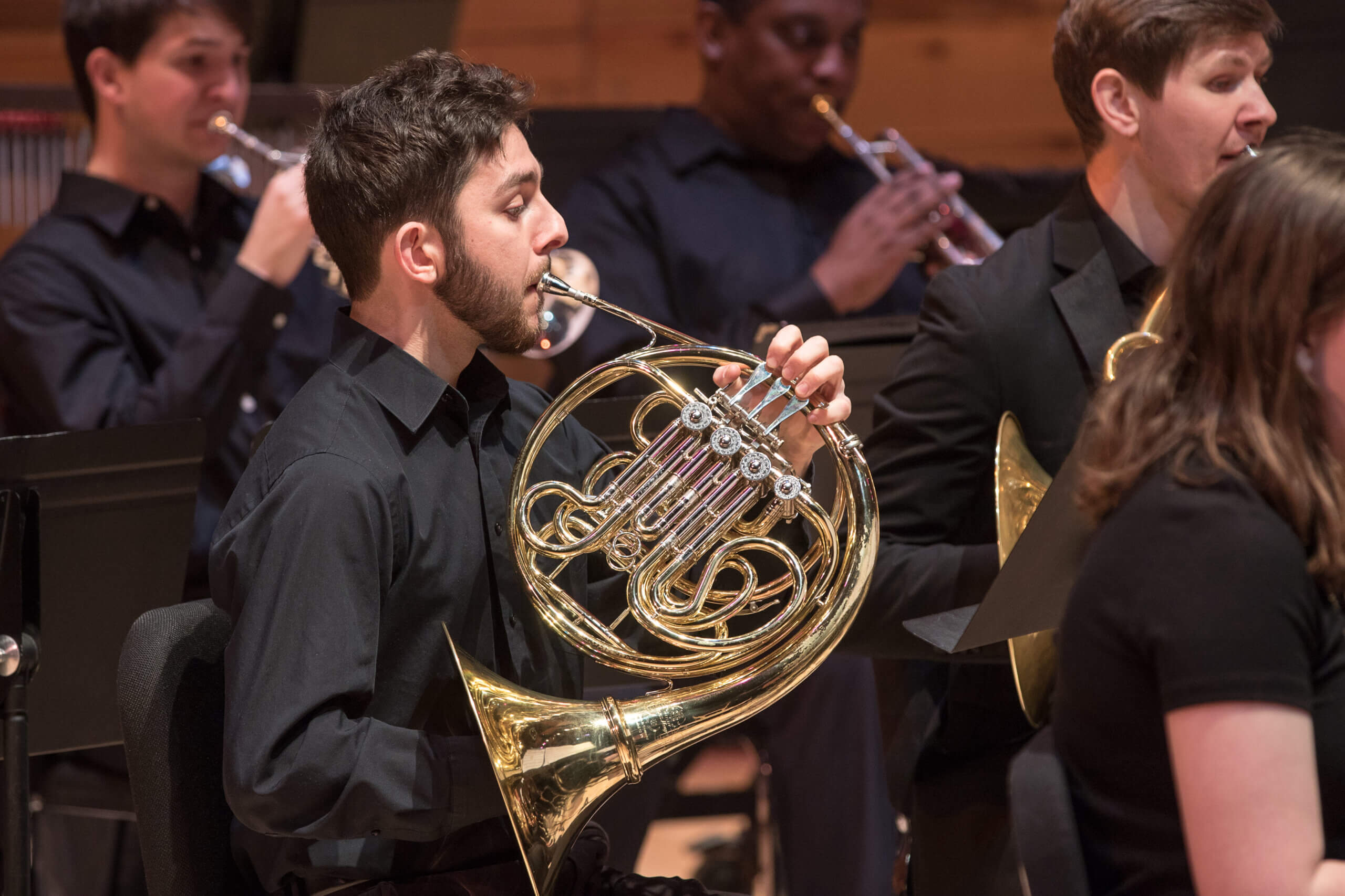 A student plays the French horn on stage. 