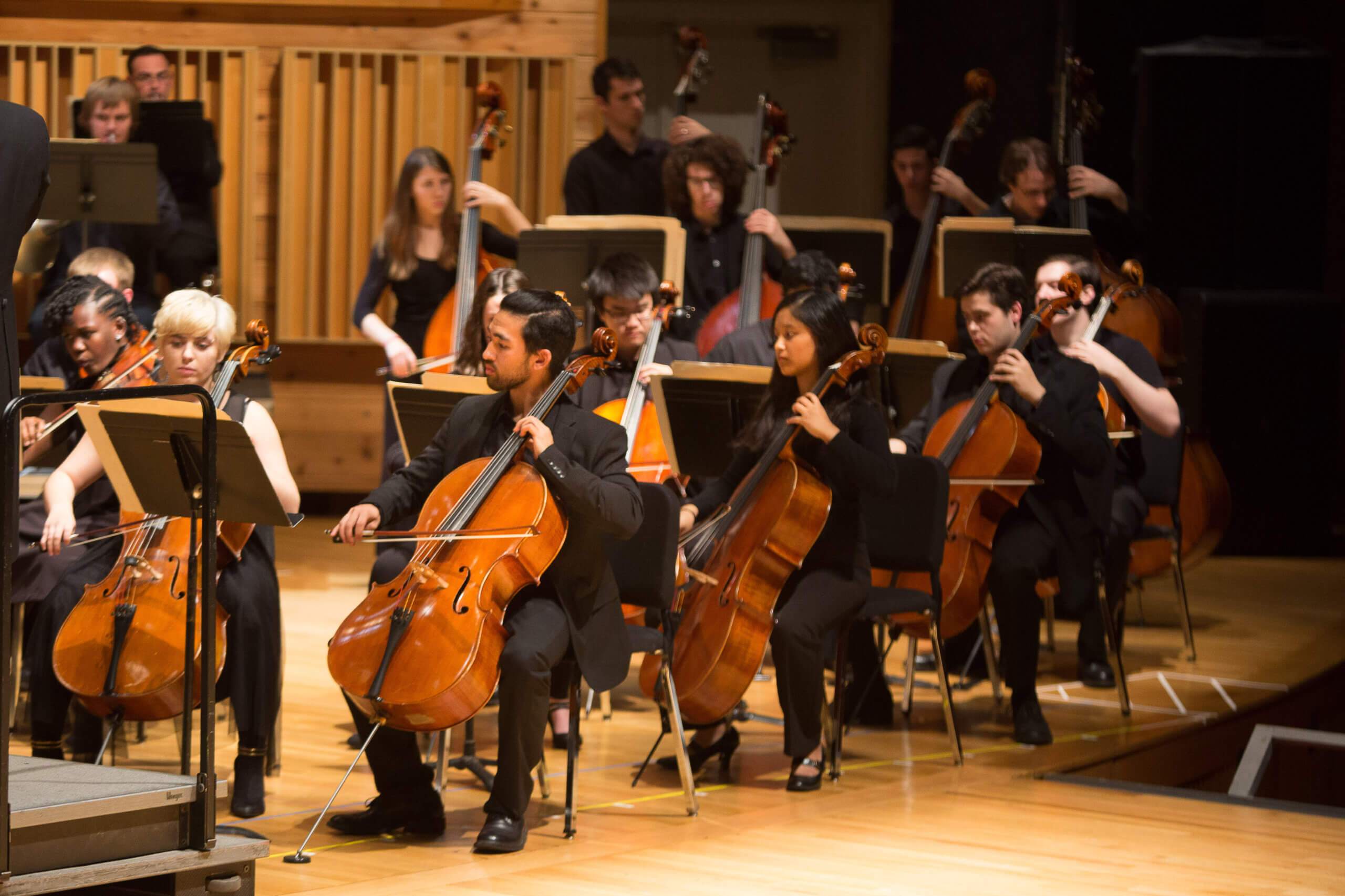 A group of students play the cello on stage. 