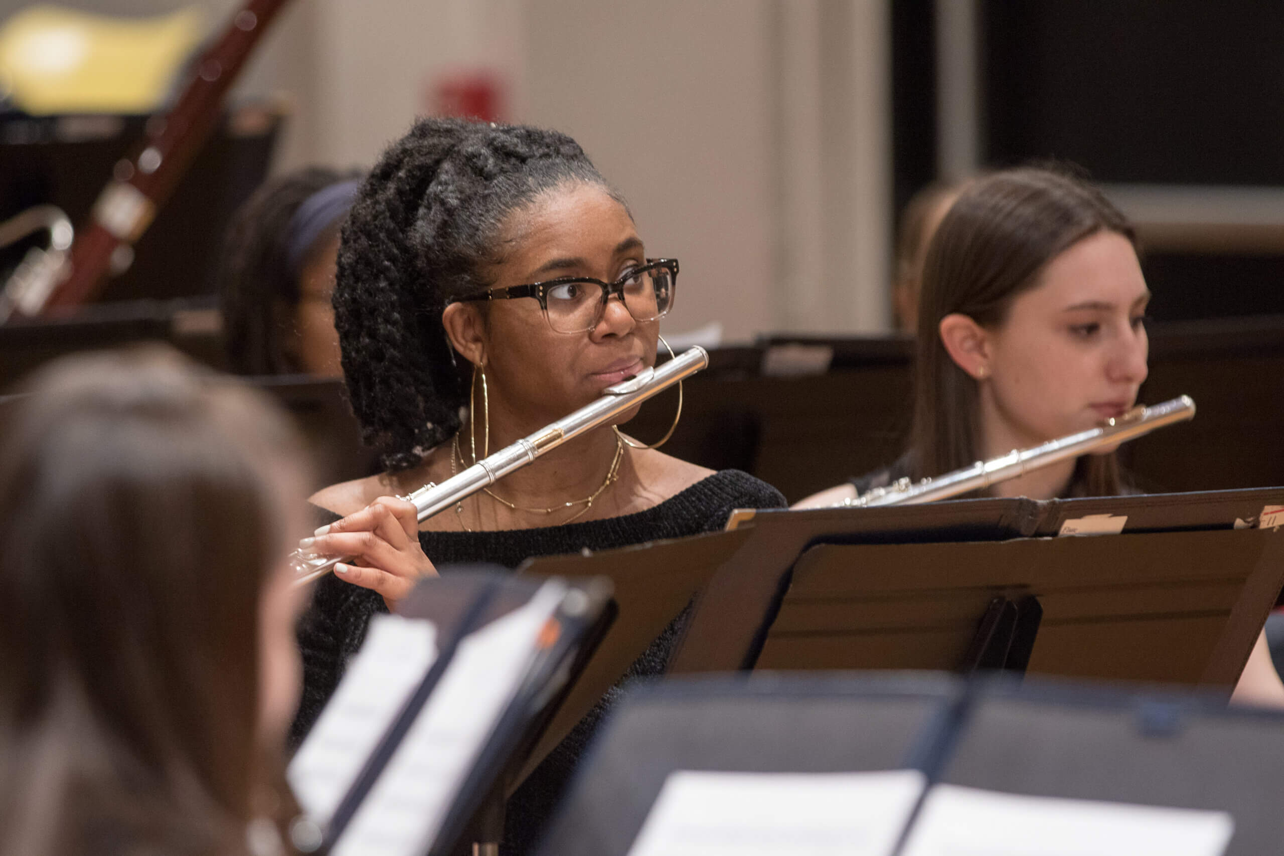 A student plays the flute in front of a music stand. 