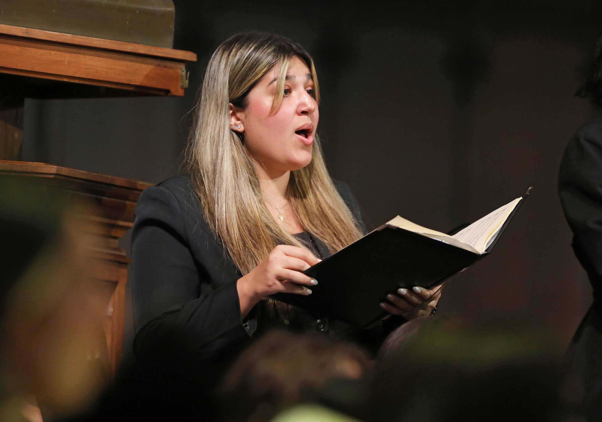 A student sings with a choir, holding a sheet music folder. 